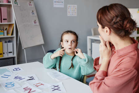 Little schoolgirl learning to read English words together with the teacher while they studying at desk in the classroomの写真素材