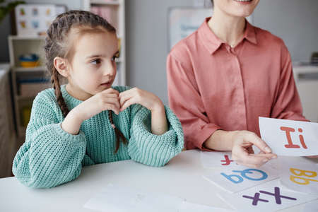 Little girl sitting at the table with teacher and learning English during a lessonの写真素材