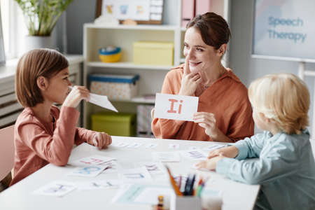 Young woman sitting at the table with children showing the card with letter and teaching them to readの写真素材