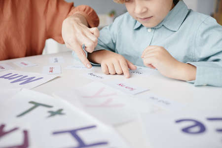 Schoolboy sitting at the table and learning to read English words together with teacher who pointing at textの写真素材
