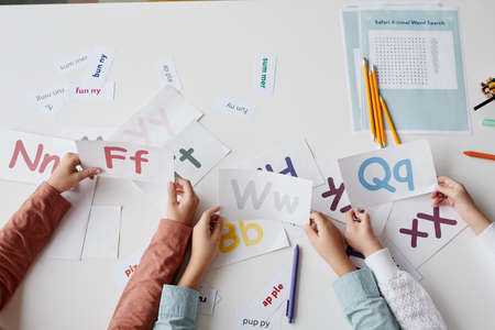Close-up of children sitting at the table together with cards and learning English alphabetの写真素材