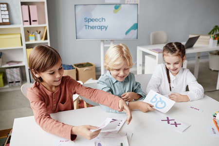Group of school children making words from cards with English letters together at the table during a lessonの写真素材