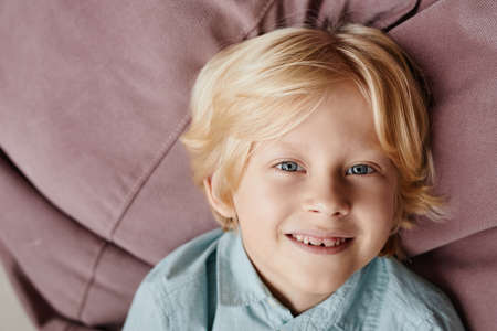 Close-up of cute little boy with blond hair smiling at camera while lying on the sofa and smilingの写真素材
