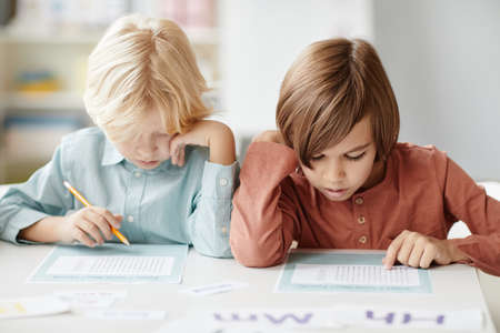 School children making notes on paper while sitting at the table during lessonの写真素材