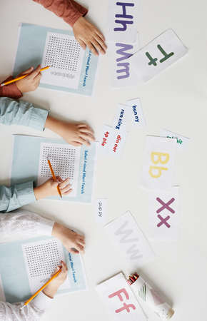 High angle view of group of children sitting at the table with English words and doing task on papersの写真素材