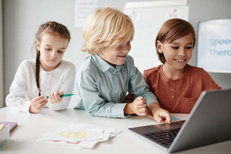 Group of children sitting at the table and typing on laptop during a lesson, they studying onlineの写真素材