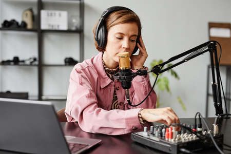Portrait of young woman speaking to microphone while recording podcast in studioの写真素材