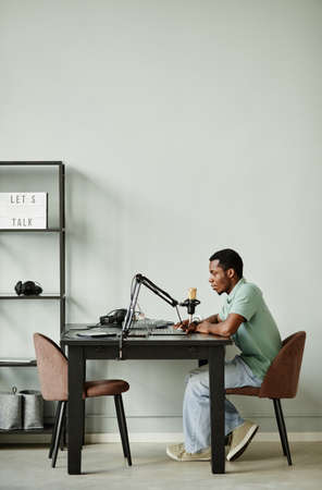 Full length side view portrait of African-American man speaking to camera while recording podcast at homeの写真素材