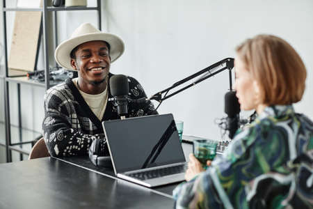 Portrait of two people speaking to microphones while recording podcast in studio