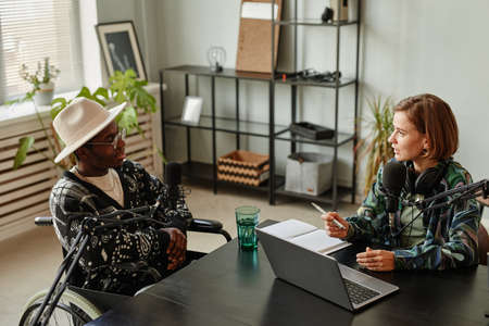 High angle portrait of African-American person in wheelchair giving interview while recording podcast in studioの写真素材