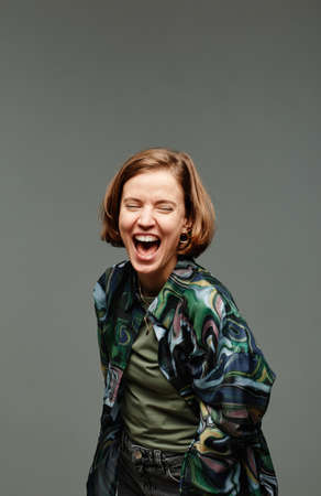 Vertical portrait of young girl laughing in studio against grey background