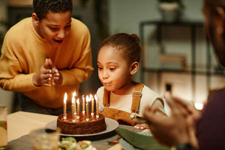 Portrait of cute little girl blowing candles on Birthday cake while celebrating with big happy familyの写真素材
