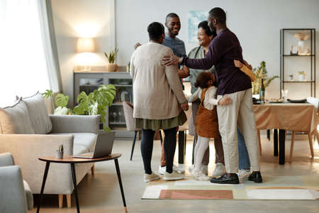 Full length portrait of big African-American family embracing while welcoming guests for dinner party at homeの写真素材