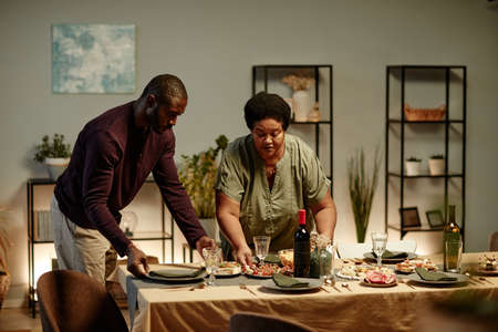 Waist up portrait of two African-American people serving table for family dinner party at home, copy...