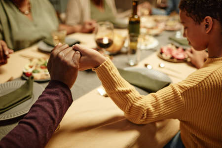 Close up of African-American family holding hands while saying grace during dinner party at homeの写真素材
