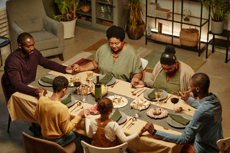 High angle view at big African-American family holding hands while saying grace during dinner party at homeの写真素材
