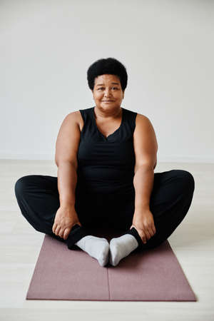 Vertical full length portrait of active senior woman sitting in lotus position while enjoying yoga...