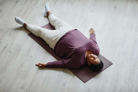 Top view portrait of black senior woman lying on floor with eyes closed while enjoying relaxation exerciseの写真素材