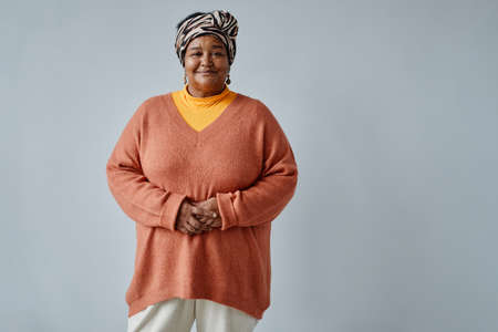 Waist up portrait of black senior woman wearing ethnic prints and looking at camera smiling against white background, copy spaceの写真素材