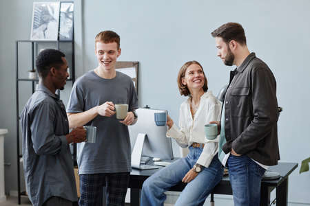 Group of business people drinking coffee from cups and talking to each other during coffee break at...