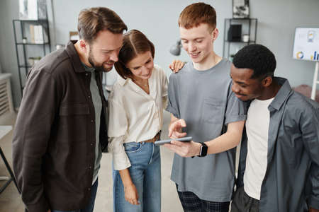 Group of young designers discussing online presentation on mobile phone in team at officeの写真素材