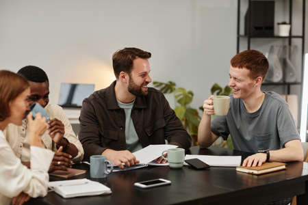 Business colleagues talking drinking coffee and laughing at the table during a meeting at office
