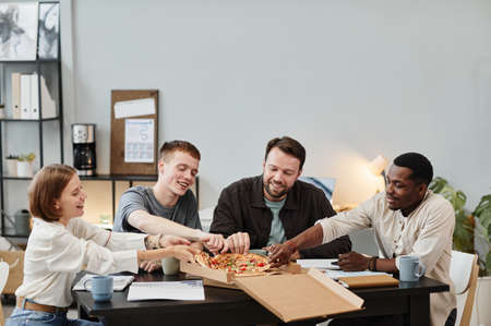 Young business people ordering pizza for lunch at office, they sitting at the table and enjoying their mealの写真素材