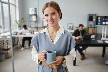 Portrait of young businesswoman drinking coffee during her break at office and smiling at camera