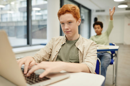 Portrait of red haired teenage boy using laptop in coding class for children, copy spaceの写真素材