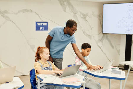 Portrait of young African-American teacher working with kids in modern school classroom, copy spaceの写真素材