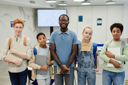 Portrait of male African-American teacher standing with diverse group of children in class and all looking at cameraの写真素材