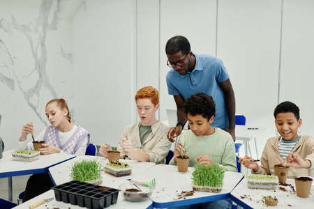 Diverse group of children planting seeds while experimenting at biology class in school with...
