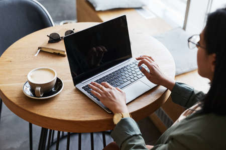 Close up of young Asian woman using laptop in cafe while working remotely in elegant wooden interior, copy spaceの写真素材