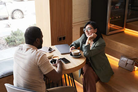 Portrait of two young people chatting at table during coffee break in graphic cafe interior, copy spaceの写真素材