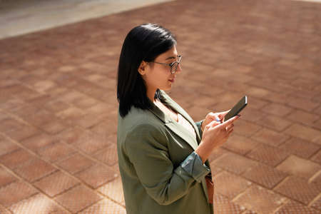 Minimal side view portrait of young businesswoman using smartphone in urban city street, copy space
