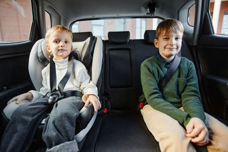Portrait of two boys sitting in back seat of family car with safety belts and looking at cameraの写真素材