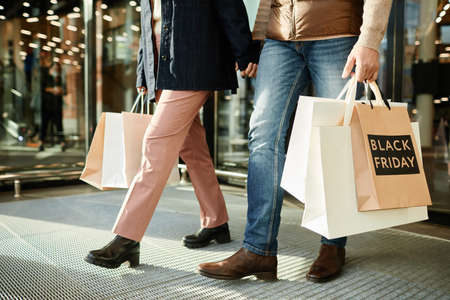 Cropped shot of unrecognizable couple holding shopping bags with Black Friday sale sign while...
