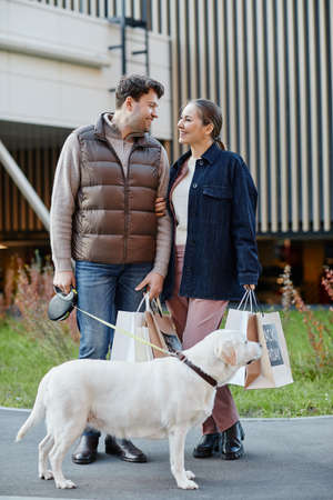 Vertical full length portrait of smiling adult couple holding shopping bags with Black Friday...