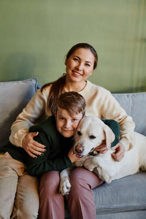 Vertical portrait of happy mother embracing son and dog in cozy home interior against green wall