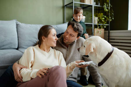 Portrait of loving family with pet dog in cozy home interior, focus on dog giving pawの写真素材