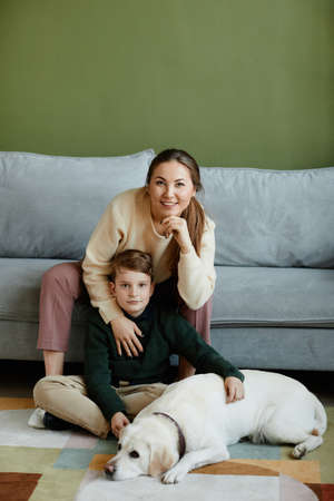 Vertical full length portrait of mother and son with pet dog in home interiorの写真素材