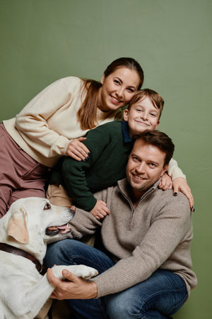 Vertical portrait of loving family with son and dog smiling at camera against green backgroundの写真素材