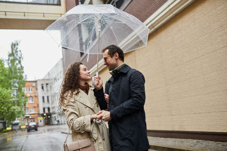 Horizontal medium portrait of Caucasian man and woman spending time together outdoors walking under umbrella and chattingの写真素材