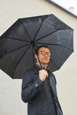 Vertical low angle medium shot of handsome Caucasian man wearing eyeglasses standing outdoors under...