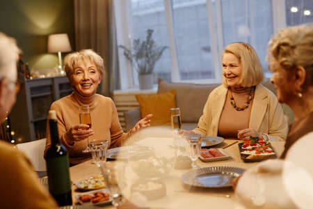 Group of senior friends gathered at dining table and having festive dinner. Beautiful aged woman...