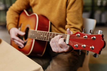 Close up of unrecognizable man wearing casual clothes sitting at table and playing acoustic guitar
