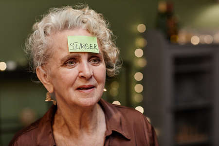 Portrait of beautiful aged woman with piece of paper on her forehead playing guessing gameの写真素材