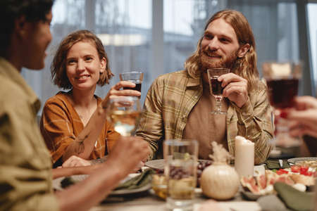 Group of young happy people drinking wine and talking to each other while they sitting at dining...