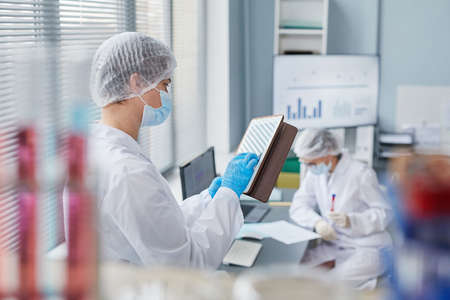Young scientist in lab coat typing on digital tablet and working online while standing in the lab