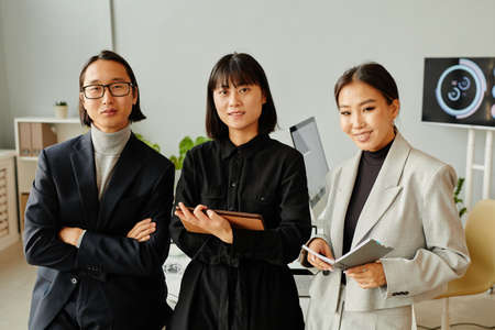 Front view portrait of young Asian business team looking at camera while standing in officeの写真素材